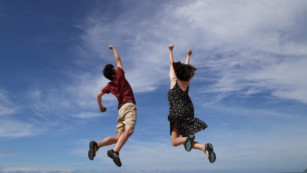 男性と女性が青空に向かってジャンプ